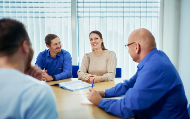 A group of people having a meeting in a bright office space. A woman and a man are smiling at each other, while two other participants are listening.